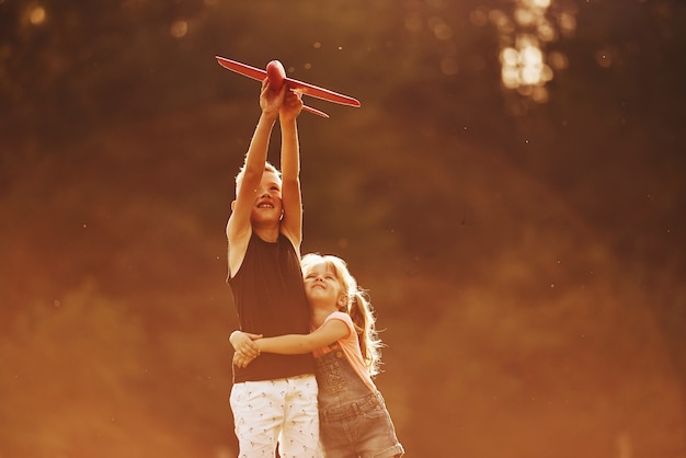 Menina e menino se divertindo ao ar livre com o avião de brinquedo vermelho nas mãos.