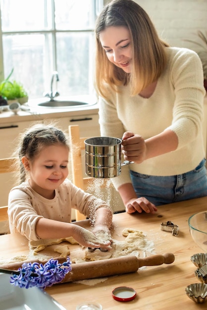 Menina e mulher cozinham em casa em uma cozinha uma criança mexe farinha na mesa com a mão bebê ajuda mãe