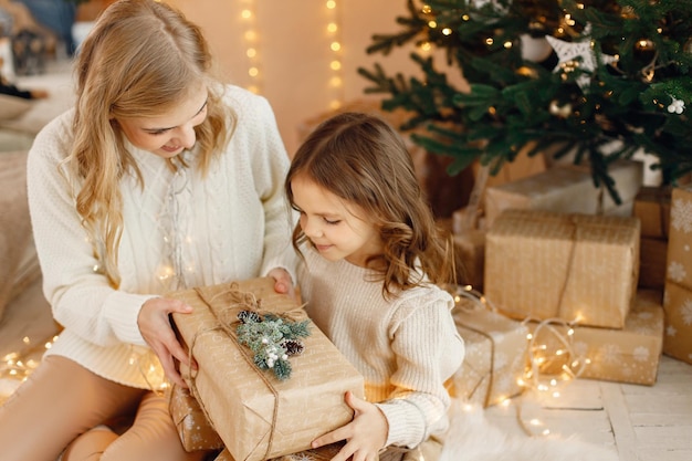 Menina e sua mãe sentada perto da árvore de Natal com caixa de presente