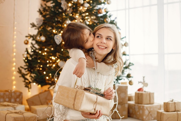 Menina e sua mãe sentadas perto da árvore de Natal e abraçando