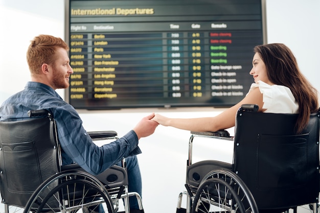 Menina e um cara em cadeiras de rodas perto do horário dos voos.