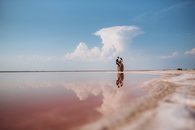 Menina e um cara na margem de um lago de sal rosa ao pôr do sol