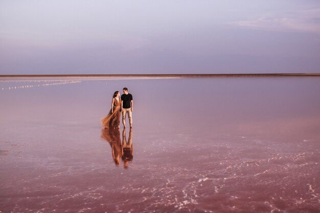 Menina e um cara na margem de um lago de sal rosa ao pôr do sol