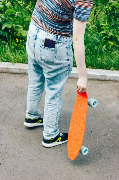 Menina elegante carregando penny board e seu smartphone no bolso do jeans no parque da cidade de verão.