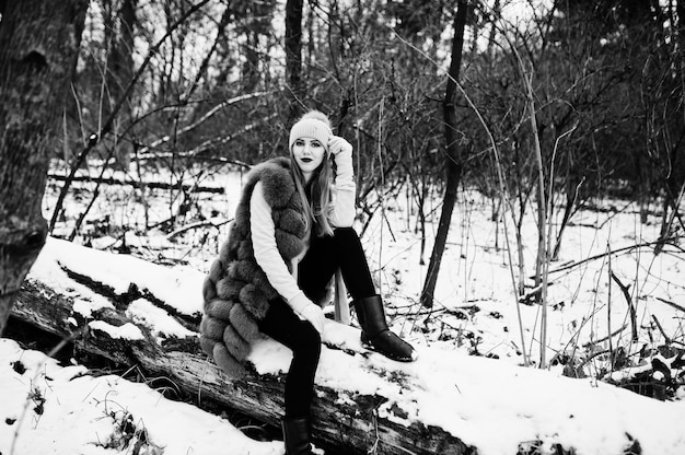 Menina elegante com casaco de pele e chapéus na floresta de inverno.