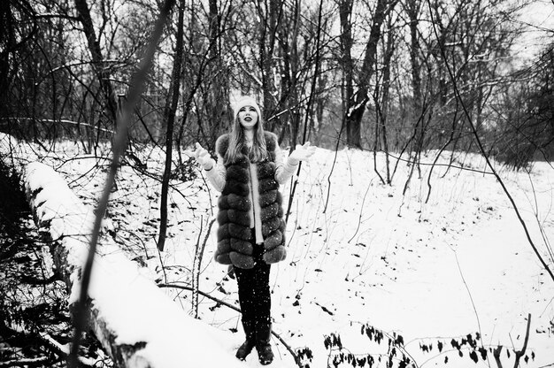 Menina elegante com casaco de pele e chapéus na floresta de inverno.