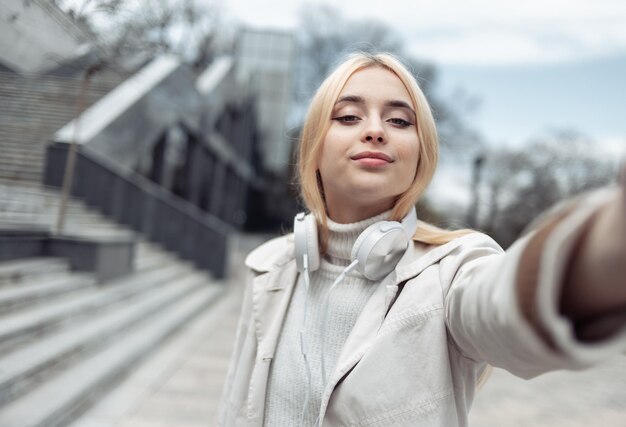 Menina elegante com fones de ouvido faz selfie ao ar livre