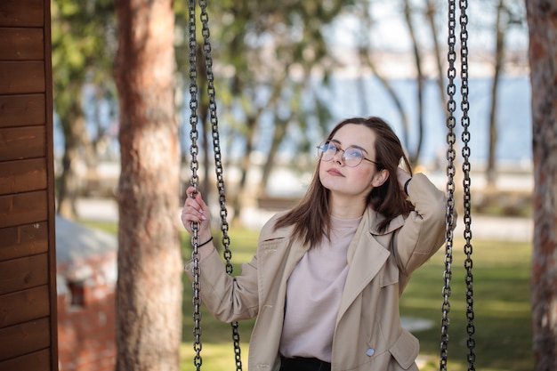 Menina elegante com óculos, ao ar livre. Menina adolescente em um balanço, retrato bonito.