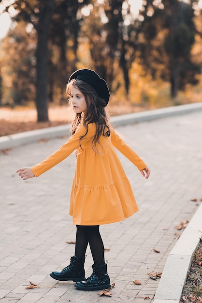 Menina elegante de 56 anos usa vestido amarelo e chapéu de boina dançando no parque de outono ao ar livre outono infância