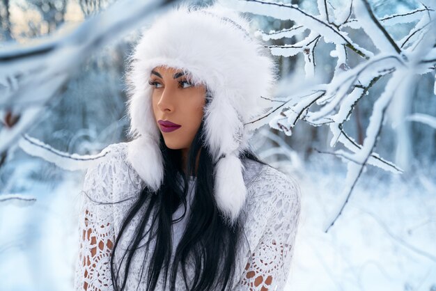 Menina elegante de chapéu quente na floresta de inverno.