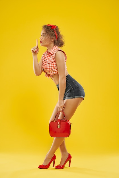 Foto menina elegante em sapatos de salto vermelho com pequena bolsa vermelha.