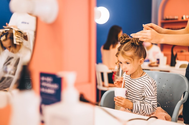 Menina elegante em um salão de beleza para crianças onde ela fez um lindo penteado estilista feminina faz um penteado elegante para menina