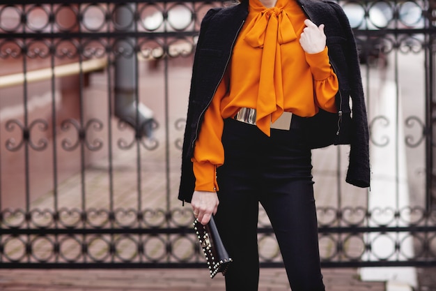 Menina elegante em um terno preto e blusa laranja fica perto da cerca