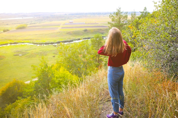 Menina elegante hippie em pé na colina da montanha. mulher feliz, apreciando a natureza do outono. paisagem bonita. conceito de viagens de estilo de vida. suéter vermelho escuro. folhas amarelas nas árvores.