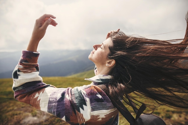 Foto menina elegante hipster com mochila e cabelo ventoso no topo das montanhas retrato de uma jovem feliz relaxando humor despreocupado incrível momento atmosférico