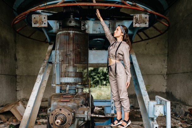 Menina elegante jovem posando perto de velho mecanismo ao ar livre.