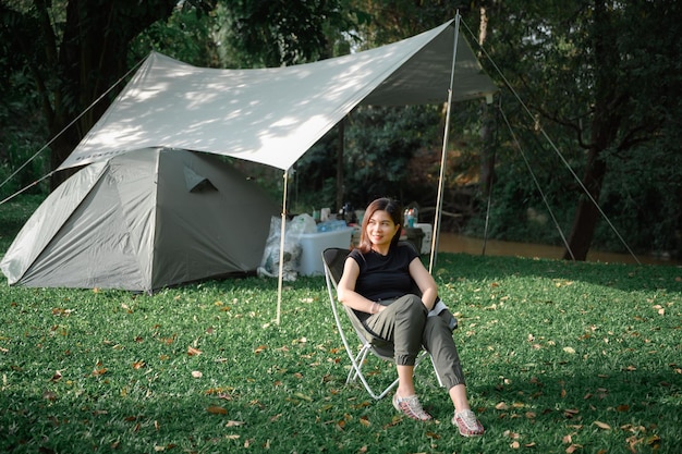 Menina elegante sentada em uma cadeira de gramado descansar nas férias Turistas femininas gostam de viajar, ir acampar barracas e dormir em florestas naturais