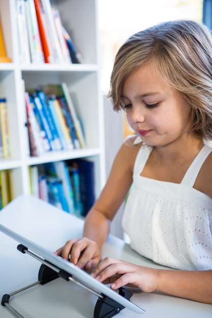 Menina elementar usando tablet digital na biblioteca