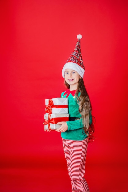 Menina elfa com presentes Ajudante do Papai Noel em um fundo de cor vermelha brilhante Copiar espaço