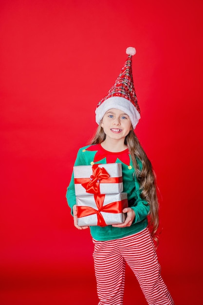 Menina elfa com presentes Ajudante do Papai Noel em um fundo de cor vermelha brilhante Copiar espaço