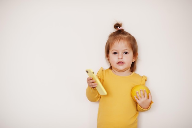 Menina em amarelo com limão e telefone celular, fundo isolado.