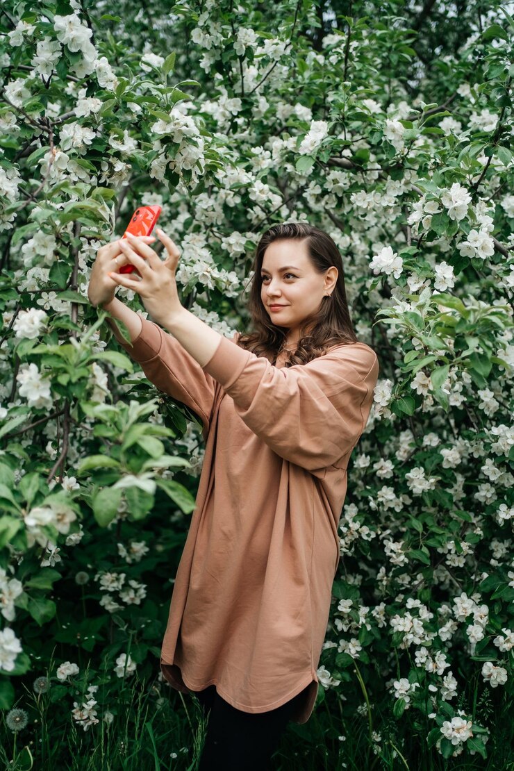 Foto menina em árvore de maçã florescente usando smartphone chamada de vídeo natureza ao ar livre