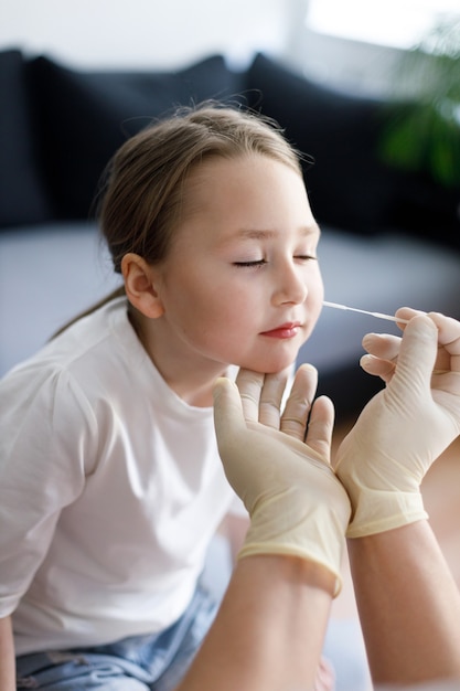 Menina em casa durante a coleta de amostra de teste de muco nasal do nariz realizando procedimento de teste de vírus respiratório mostrando Covid-19