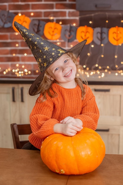 Menina em casa na cozinha à mesa com uma abóbora para o halloween