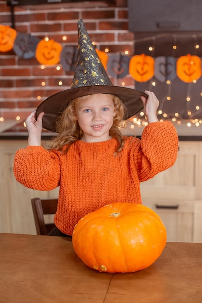 Menina em casa na cozinha à mesa com uma abóbora para o halloween