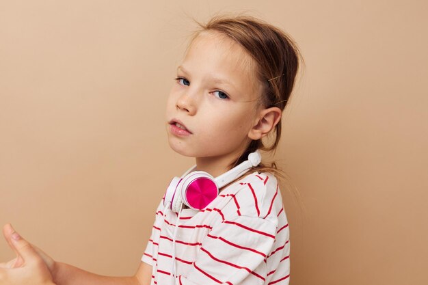 Menina em fones de ouvido de camiseta listrada gesto mãos fundo bege