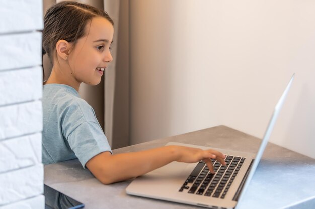 Menina em idade escolar está estudando em casa. uma garota assiste a uma vídeo aula em um monitor de laptop e escreve tarefas em um notebook.