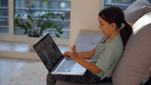 Menina em idade escolar está estudando em casa. Uma garota assiste a uma vídeo aula em um monitor de laptop e escreve tarefas em um notebook.