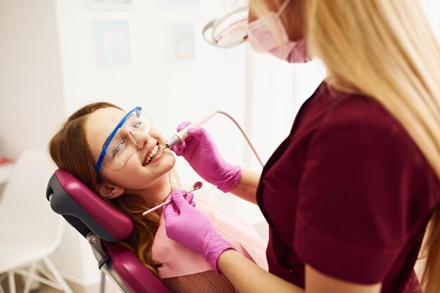 Menina em óculos de proteção visitando dentista na clínica Concepção de estomatologia