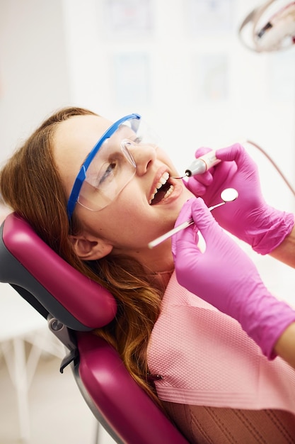 Menina em óculos de proteção visitando dentista na clínica Concepção de estomatologia