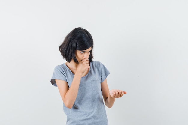 Menina em t-shirt fingindo segurar algo e olhando pensativa, vista frontal.