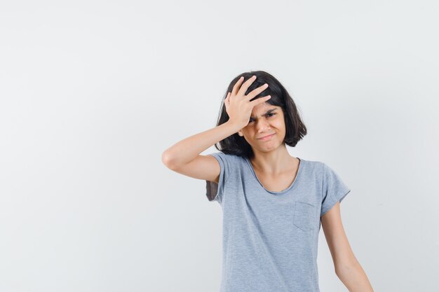 Menina em t-shirt, segurando a mão na cabeça e olhando arrependido, vista frontal.