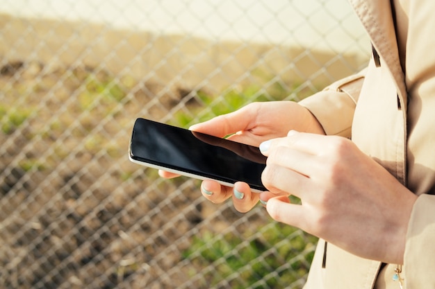 Menina em um casaco bege andando na rua e usa telefone celular em um dia ensolarado