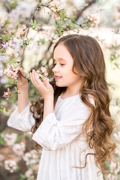 Menina em um jardim de floração de primavera. a criança olha as flores brancas.