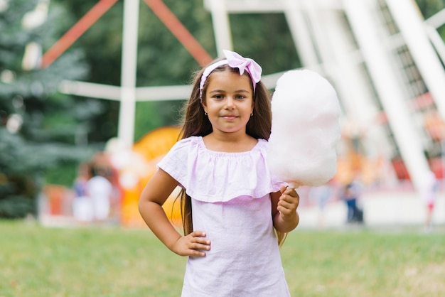 Menina em um parque de diversões no verão come algodão doce e sorri alegremente