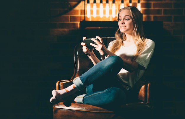 Menina em um quarto escuro acolhedor, segurando um telefone