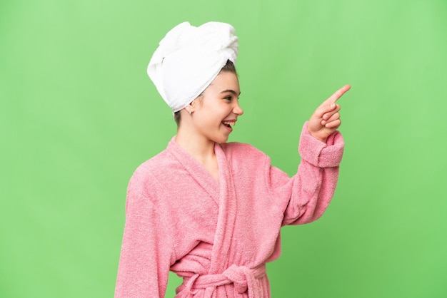 Menina em um roupão de banho sobre fundo croma chave isolado apontando para fora