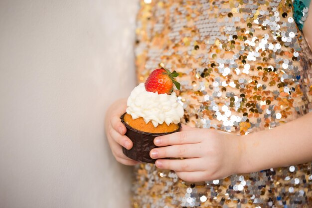 Menina em um vestido brilhante segurando um lindo cupcake de perto