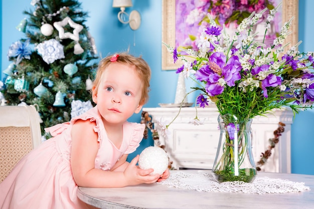 Menina em um vestido comemorativo joga perto da árvore de Natal