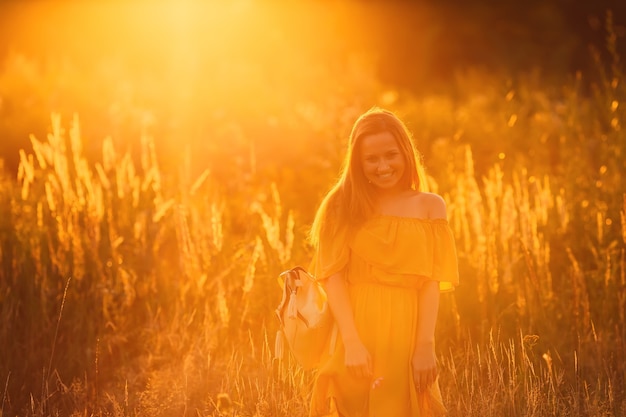 Menina em um vestido elegante e uma mochila no ombro no contexto do pôr do sol