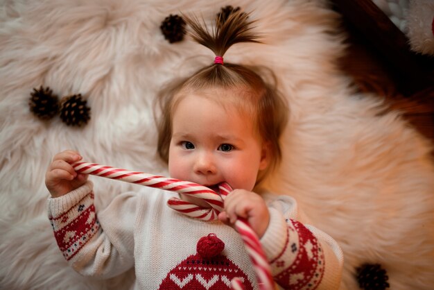 Menina em uma fantasia de Natal vermelha com guirlandas retrô senta-se em uma pele