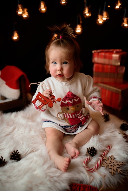 Foto menina em uma fantasia de natal vermelha com guirlandas retrô senta-se em uma pele