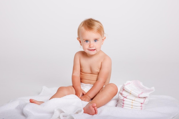 Menina em uma fralda com uma pilha de fraldas em um fundo branco