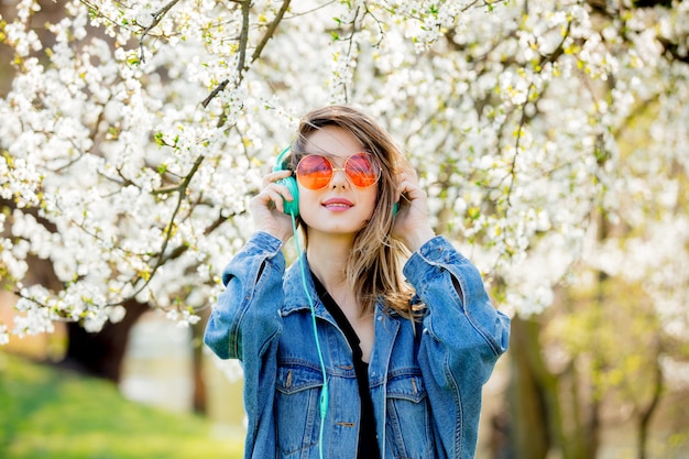 Foto menina em uma jaqueta jeans e fones de ouvido perto de uma árvore de florescência