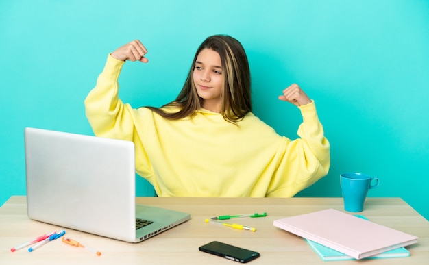 Foto menina em uma mesa com um laptop sobre um fundo azul isolado fazendo um gesto forte