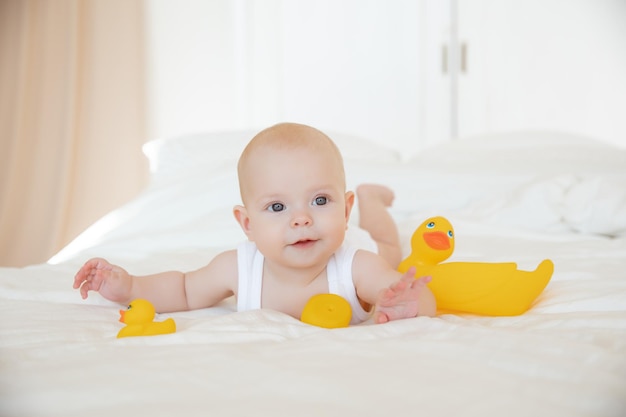 Menina em uma roupa branca deitada na cama brincando com patos de borracha